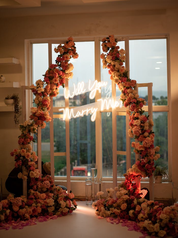 Floral arch with Will You Marry Me neon sign, ideal for romantic proposals.